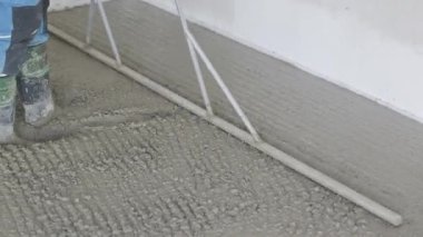 İnşaat işçisi ıslak beton yüzeyi alüminyum boğayla düzleştiriyor.