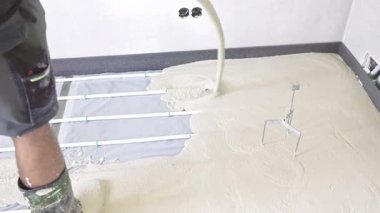 İnşaat işçisi zeminin altındaki ısıtma sistemine beton döküyor.