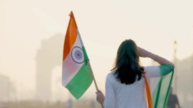 Proud Indian girl saluting at India gate with Indian flag in hand