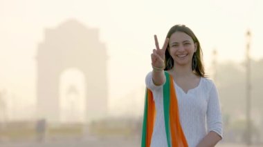 Happy Indian girl showing Victory sign at India gate in an Indian wear