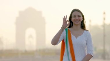 Happy Indian girl showing Okay sign at India gate in an Indian wear