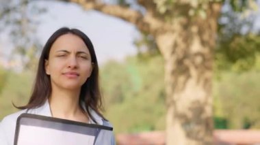 Confident Indian employee walking in a park with files and folders in hand