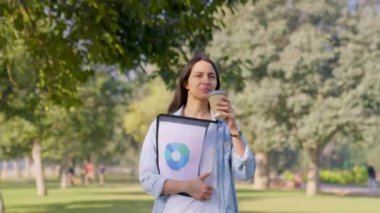 Happy Indian employee walking in a park with coffee mug in hand