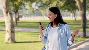 Indian girl walking and enjoying music in wireless earphones at a college park