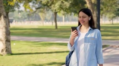 Indian girl listening and enjoying to music in wireless earphones at a park