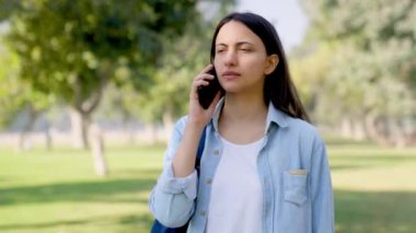 Serious Indian girl talking on a call in a park in daylight