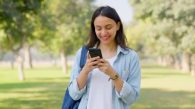 Happy Indian girl texting and chatting with someone in a park