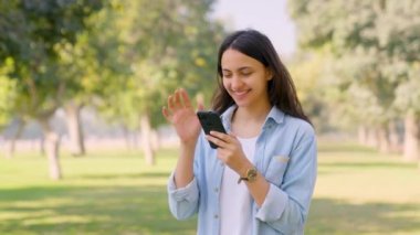 Happy Indian girl using mobile phone in a park and smiling