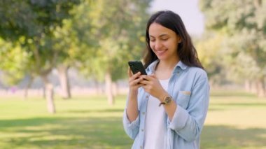 Happy Indian girl messaging someone using mobile phone through texting and chatting