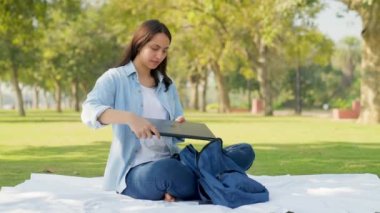 Indian college girl taking out laptop from her backpack in a park to study and do observation