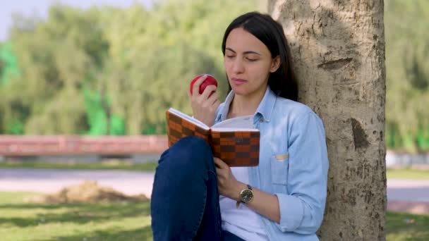 Индийская Девушка Ест Яблоко Время Чтения Книги Парке — стоковое видео