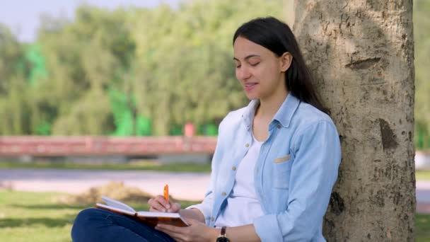 Intelligent Indian Girl Writing Something Notebook Sitting Park Tree — Wideo stockowe
