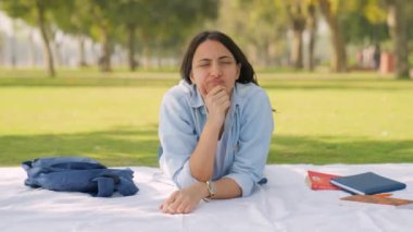 Confused and intelligent Indian girl thinking while lying down in a park