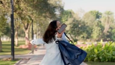 Happy Indian college girl dancing and grooving in a pak while listening to music through wireless earphones