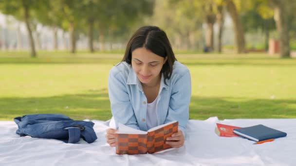 Happy Indian Girl Reading Book While Lying Park — Vídeo de Stock