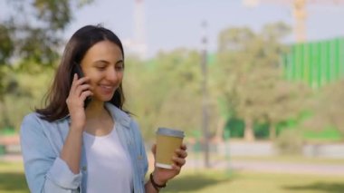 Happy Indian girl talking on a phone while walking in a park
