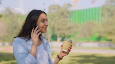 Happy Indian girl talking on a phone while walking in a park in sunlight