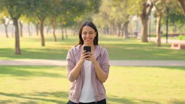 一个快乐的印度女孩早上在公园里用手机过冬 — 图库视频影像