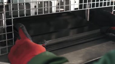 Metal işçiliği yapan bir makine, bir metal levhayı dikdörtgen şeklinde keser. Eldiven giyen bir işçi ise kuru sıkı monte eder. Otomatik Metal Katlama ve Bükme Makinesi. Üretim süreci. Hassas Makine. Kapat.