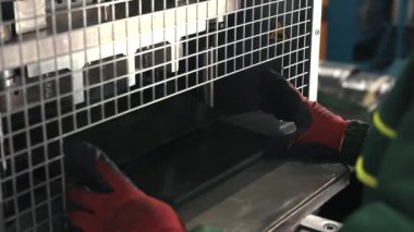 Metal işçiliği yapan bir makine, bir metal levhayı dikdörtgen şeklinde keser. Eldiven giyen bir işçi ise kuru sıkı monte eder. Otomatik Metal Katlama ve Bükme Makinesi. Üretim süreci. Hassas Makine. Kapat.