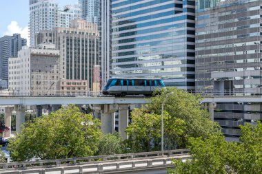 Miami, Florida, ABD - 12 Mayıs 2019: Miami şehir merkezinde arka planda şehir binaları olan hareket halindeki bir Metromover treni. Metromover ücretsiz bir toplu taşıma. Otomatik insan taşımacılığı tren sistemi..