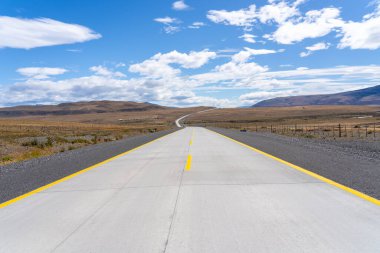Şili 'deki Atacama Çölü' nü geçen sarı çizgilerle dolu uzun düz bir yol. Mavi gökyüzünde bulutlu güneş.