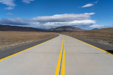Şili 'deki Atacama Çölü' nü geçen dağlara doğru giden sarı çizgileri olan uzun bir yol. Mavi gökyüzünde bulutlu güneş.