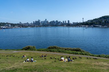 Seattle, WA, United States - June 15, 2023: People relaxing on the beach at Gas Works Park and enjoying a view of the Seattle skyline. Seattle, WA, United States. clipart