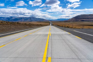 Şili 'deki Atacama Çölü' nü geçen dağlara doğru giden sarı çizgileri olan uzun bir yol. Mavi gökyüzünde bulutlu güneş.