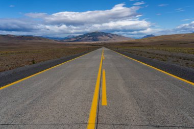 Şili 'deki Atacama Çölü' nü geçen dağlara doğru giden sarı çizgileri olan uzun bir yol. Mavi gökyüzünde bulutlu güneş.