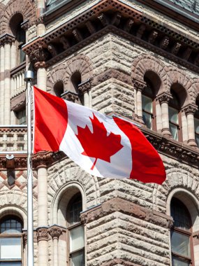 Toronto, Kanada - 16 Mayıs 2020: Toronto, Kanada 'da eski belediye binasının arka planında dalgalanan Kanada bayrağı. Toronto, Ontario eyaletinin başkenti ve Kanada 'nın en kalabalık şehridir..