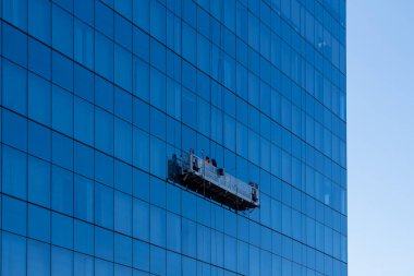 Buffalo, New York, ABD - 8 Aralık 2023: Asılı bir platformda iki pencere temizleyicisi yüksek katlı bir ofis binasının cam perde duvarını temizliyor. Buffalo, New York, ABD.