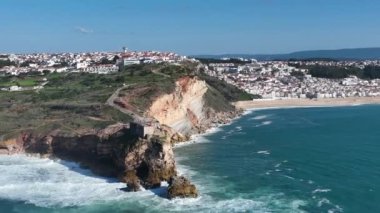 Nazare, Portekiz 'deki deniz feneri. Dalgalar ve sörf için ünlü bir yer. Plaj ve Okyanus Dalgaları Arkaplanda. 4k