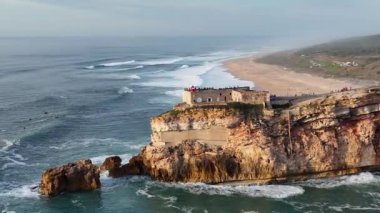 Nazare, Portekiz 'deki deniz feneri. Dalgalar ve sörf için ünlü bir yer. Plaj ve Okyanus Dalgaları Arkaplanda. 4k