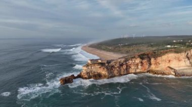Nazare, Portekiz 'deki deniz feneri. Dalgalar ve sörf için ünlü bir yer. Plaj ve Okyanus Dalgaları Arkaplanda. 4k