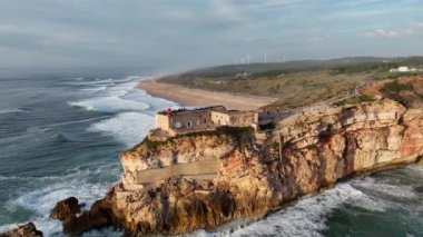 Nazare, Portekiz 'deki deniz feneri. Dalgalar ve sörf için ünlü bir yer. Plaj ve Okyanus Dalgaları Arkaplanda. 4k