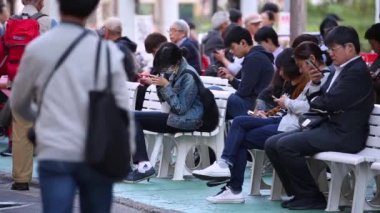 People are Sitting and Playing Mobile Games in Tokyo Public Area. Shinjuku District