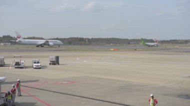 Tokyo International Narita Airport and Ground Service is Working in Background. Japan Airlines, ANA, NIppon, KLM Airplane are Taxing to Take Off. Bright Sunny Day