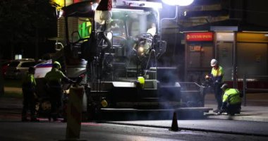 Road repair at night. Asphalt paver applying asphalt on the street. Construction of a new road. A layer of freshly laid asphalt in the city. Vilnius city, Lithuania