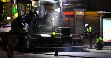 Road repair at night. Asphalt paver applying asphalt on the street. Construction of a new road. A layer of freshly laid asphalt in the city. Vilnius city, Lithuania