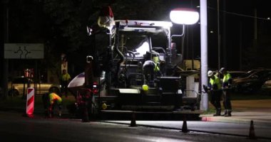 Road repair at night. Asphalt paver applying asphalt on the street. Construction of a new road. A layer of freshly laid asphalt in the city. Vilnius city, Lithuania