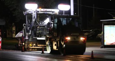 Road repair at night. Asphalt paver applying asphalt on the street. Construction of a new road. A layer of freshly laid asphalt in the city. Vilnius city, Lithuania. The road roller is laying asphalt.