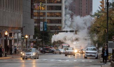 Baltimore, Maryland - October 03, 2019: Traffic in Baltimore, Maryland. USA. Hot Water Steam in Background. Downtown Street