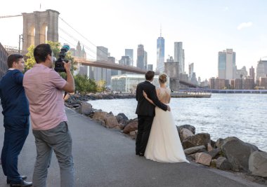 Wedding photo shoot in Brooklyn Bridge Park in NYC. Bride and Groom with Photographer and assistant. Sightseeing and picturesque place.