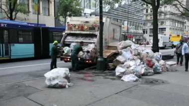 Garbage Truck in NYC and two DSNY workers Loading White Plastic Garbage Trash Bags into Truck. People on Sidewalk. Manhattan. Morning.