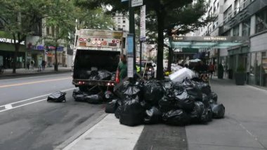 Garbage Truck in NYC and two DSNY workers Loading Black Garbage Trash Bags into Truck. Manhattan. Daytime