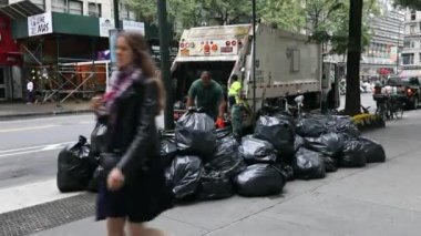 Garbage Truck in NYC and two DSNY workers Loading Black Garbage Trash Bags into Truck. Manhattan. Daytime