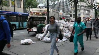 Garbage Truck in NYC and two DSNY workers Loading White Plastic Garbage Trash Bags into Truck. People on Sidewalk. Manhattan. Morning.