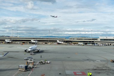 SAN FRANCISCO, CALIFORNIA - APRIL 04, 2019: San Francisco International Airport. United Airlines Boeing is Taxing and Ground Service in Background. American Airlines is Taking Off