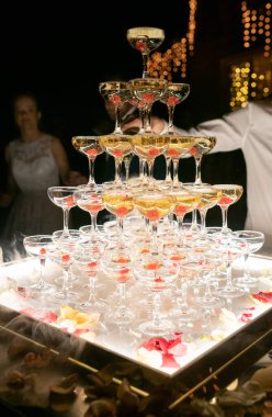 Champagne glasses standing in a tower at the wedding party. Champagne glass pyramid. Pyramid of glasses of wine, champagne, tower of champagne. Wedding party at night